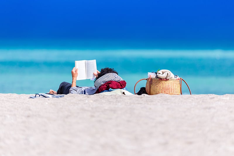 Una lettrice rilassata sulla spiaggia con il suo libro in lingua inglese