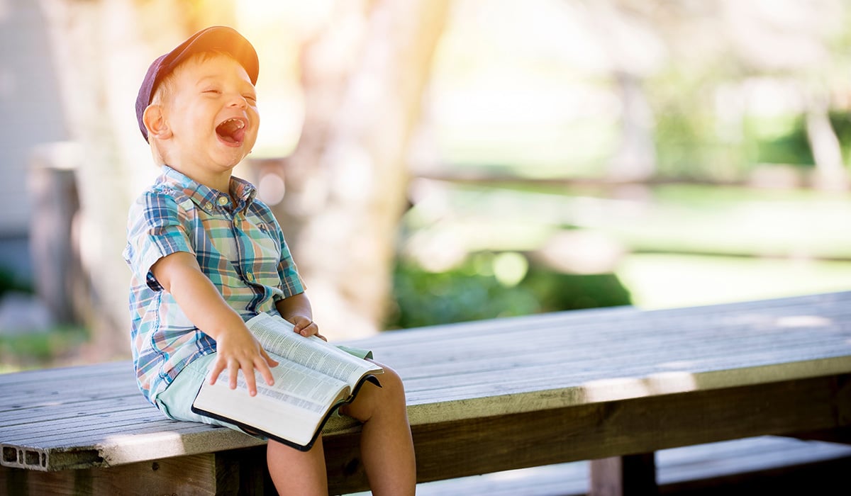 Un bambino felice ride con un libro sulle gambe